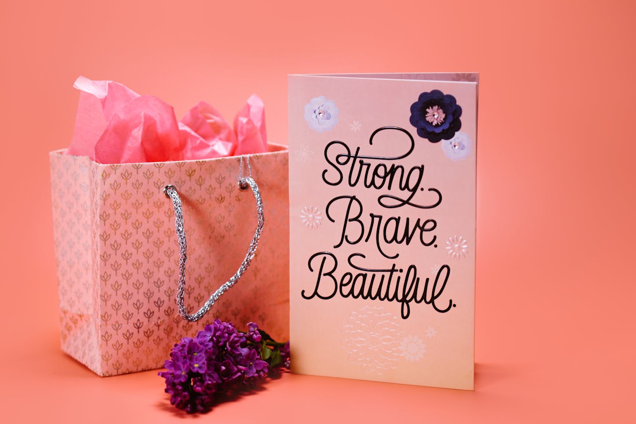 A stylish greeting card with Strong, Brave, Beautiful text alongside a floral gift bag.